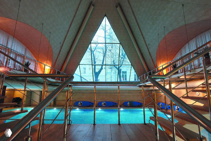 Бассейн с дорожками и панорамным окном в интерьере спортивного клуба, видна лестница и спокойная вода.