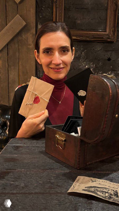 Женщина в интерьере иммерсивного ужина держит запечатанное письмо и улыбается на фоне реквизита вечеринки, атмосфера загадки и сюжета.