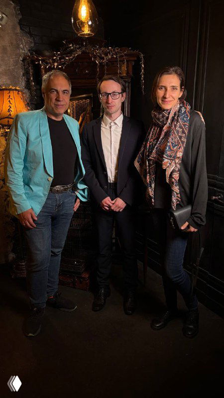 Групповое фото трёх гостей вечера на фоне тёмного антуража места проведения — участники иммерсивного перформанса после шоу.