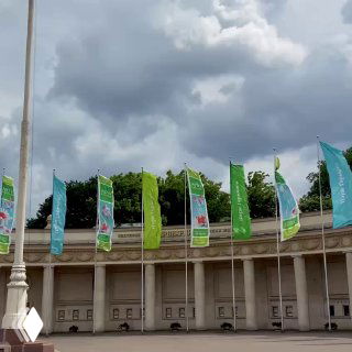 Флаги и колоннада в Парке Горького под тёмными грозовыми тучами, вид на фасад парковой постройки и развевающиеся баннеры фестиваля.