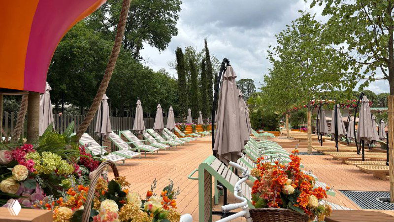 Платный пляж в Парке Горького с лежаками и зоной отдыха, оформленные цветами и зонтиками на фоне зелени и пасмурного неба.