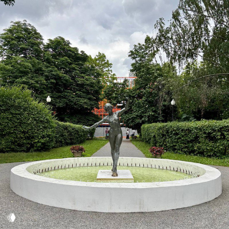 Пешеходная аллея в Парке Горького с фонтаном и скульптурой на круглом постаменте, вокруг густая зелень и дорожки.