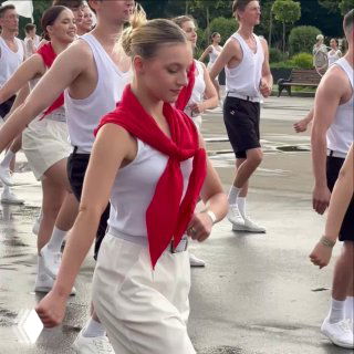 Парад физкультурников в Парке Горького: группа молодых людей в белой форме марширует по аллее при пасмурной погоде.