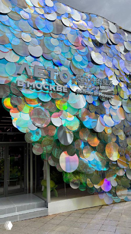 Фасад арт-павильона в Москве, покрытый большими голографическими дисками; яркие отражения города и вход в торгово-выставочную зону проекта.