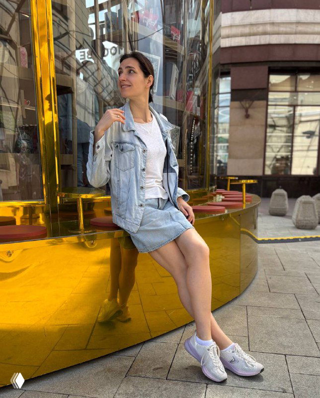 Женщина сидит на фоне большого золотого отражающего арт-объекта: прогулка по выставочным павильонам и уличным инсталляциям в центре города.