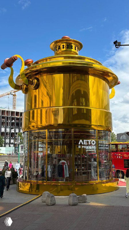 Крупный золотой арт-павильон в форме самовара на городской площади Москвы с логотипом проекта «Лето в Москве» и людьми у входа.