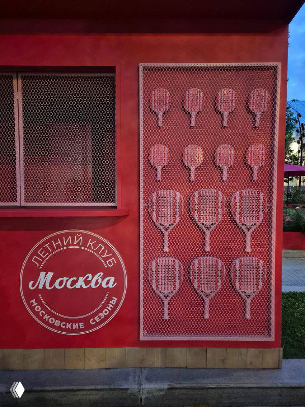 Красная декоративная стенка с графикой теннисных ракет и логотипом 'Москва' — элемент визуального оформления одного из торговых павильонов.