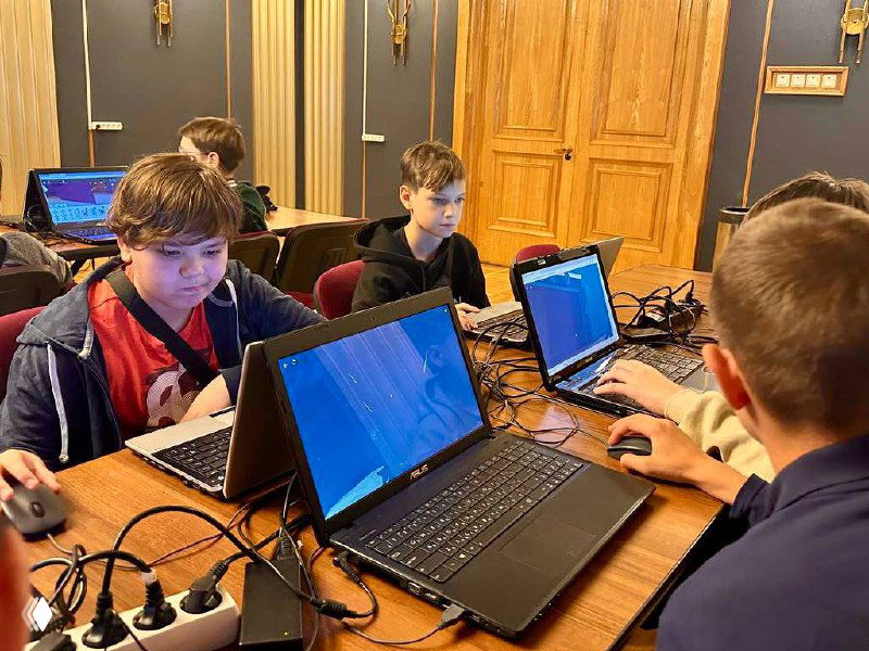 Подростки за ноутбуками в комнате с деревянной отделкой — вероятно квест или образовательная активность в рамках спортивно-образовательной смены лагеря.