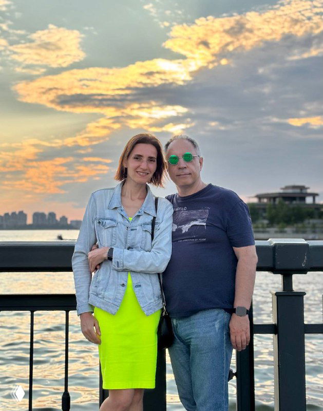 Автор поста и спутник на набережной Казанки на фоне закатного неба; пара стоит у перил, позади виднеется река и силуэт города.