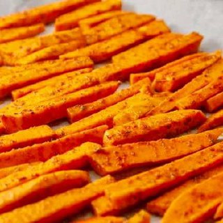 Лоток с нарезанным бататом в виде брусков, приправленным специями и оливковым маслом, готовый к запеканию на противне, крупный план