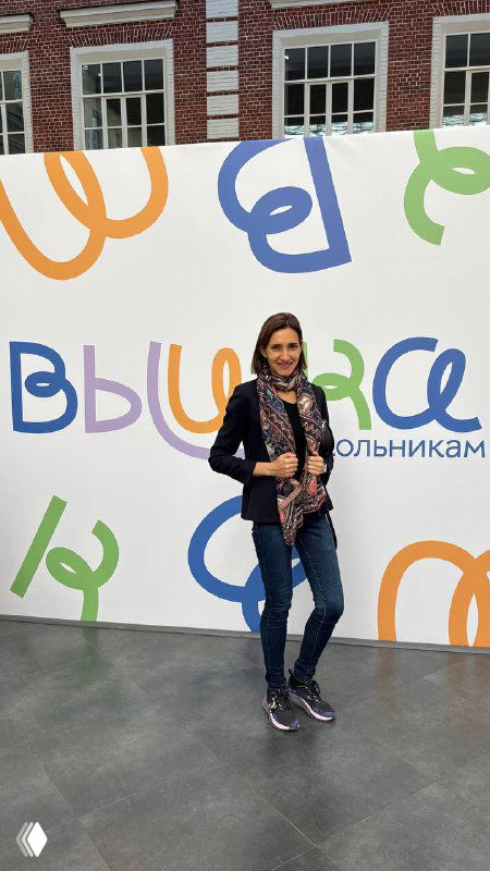 Полноформатный снимок автора на фоне брендированной фотозоны фестиваля школьников ВШЭ с яркими буквами и логотипами университета, посетители и оформление мероприятия.