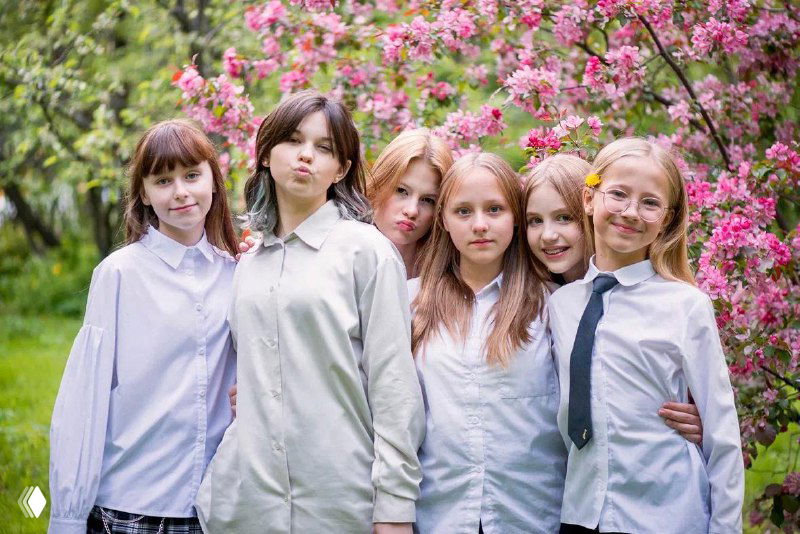 Группа школьниц на улице возле цветущих кустов — ученицы в форме или повседневной школьной одежде, дружеская компания в парковой зоне школы.