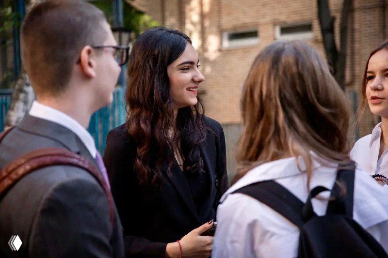 Группа старшеклассников ведёт беседу в коридоре школы — обсуждение учебных вопросов, социализация подростков и общение в учебной среде.