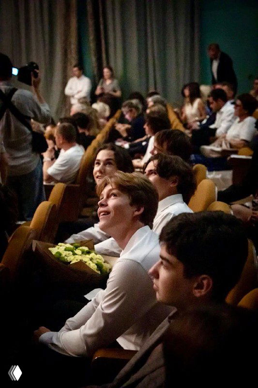 Зрители в актовом зале школы во время школьного мероприятия — родители и ученики смотрят выступление, тёплая атмосфера школьных праздников и собраний.