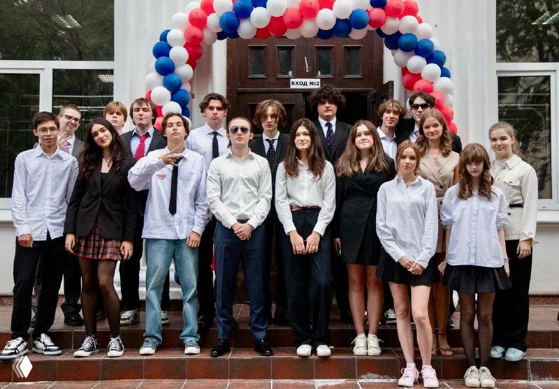 Групповая фотография старшеклассников и выпускников у входа в школу, украшенного шариками — торжественное мероприятие, атмосфера окончания учебного года.