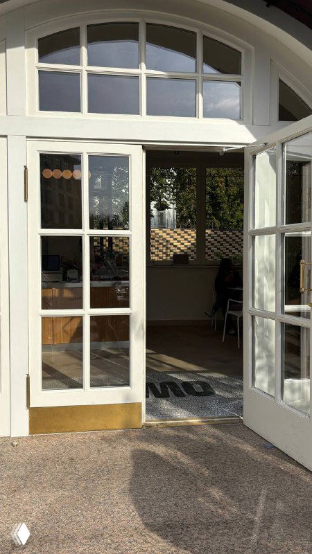 Открытая дверная арка с большими стеклянными створками: вход в кафе с белыми рамами и приглашающей атмосферой минималистичного интерьера.