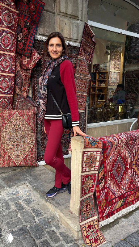 Виктория позирует у лавки с бакинскими коврами, витрина с красочными узорами, атмосфера старого рынка и рукодельных товаров