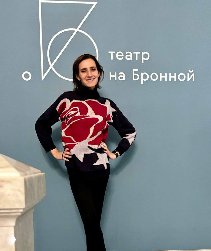 Портрет автора на фоне стены с логотипом «Театр на Бронной», поза в полный рост, атмосфера перед началом спектакля