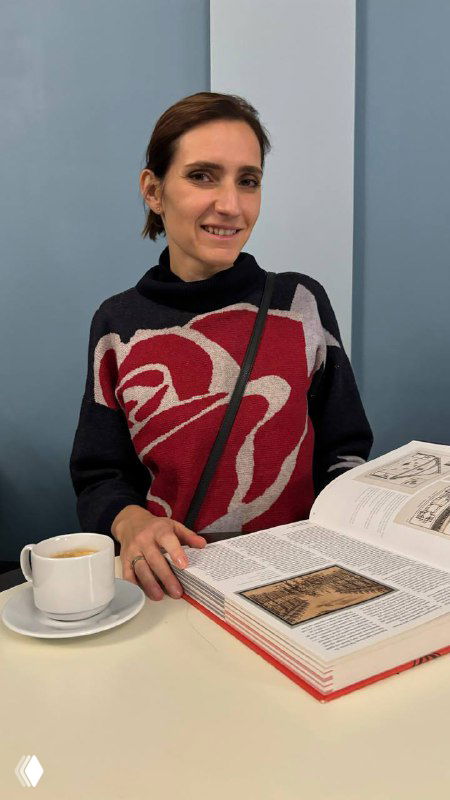 Автор за столиком в театральном кафе с чашкой и открытой книгой, размышляющая атмосфера перед или после спектакля