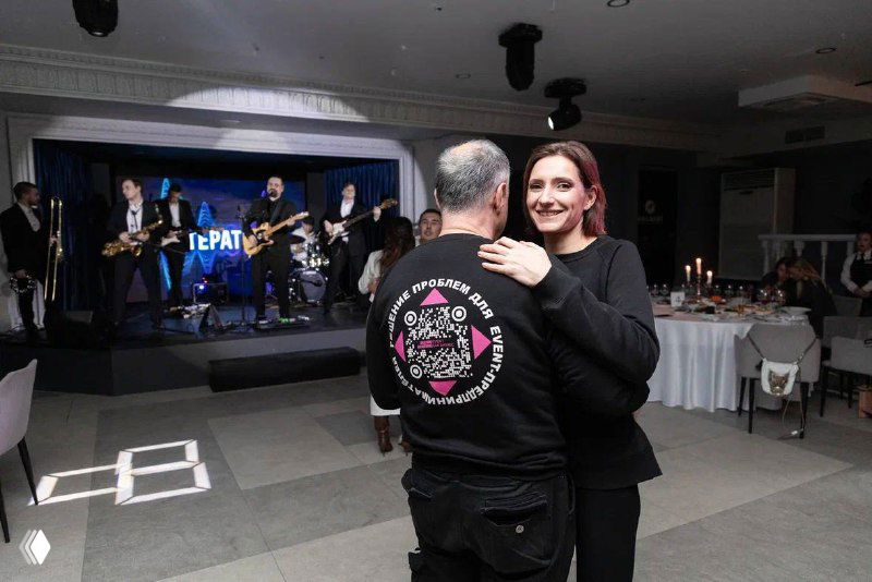 Виктория танцует или обнимается с партнёром на вечернем мероприятии форума; музыканты и праздничная сцена видны в фоне.