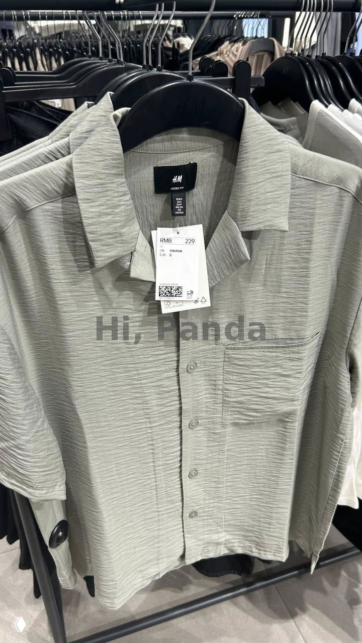 Светлая рубашка H&M на вешалке с биркой и ценником RMB 229, видно внутреннее оформление магазина и стойки с одеждой в ТЦ Mangrove Tree Sanya.