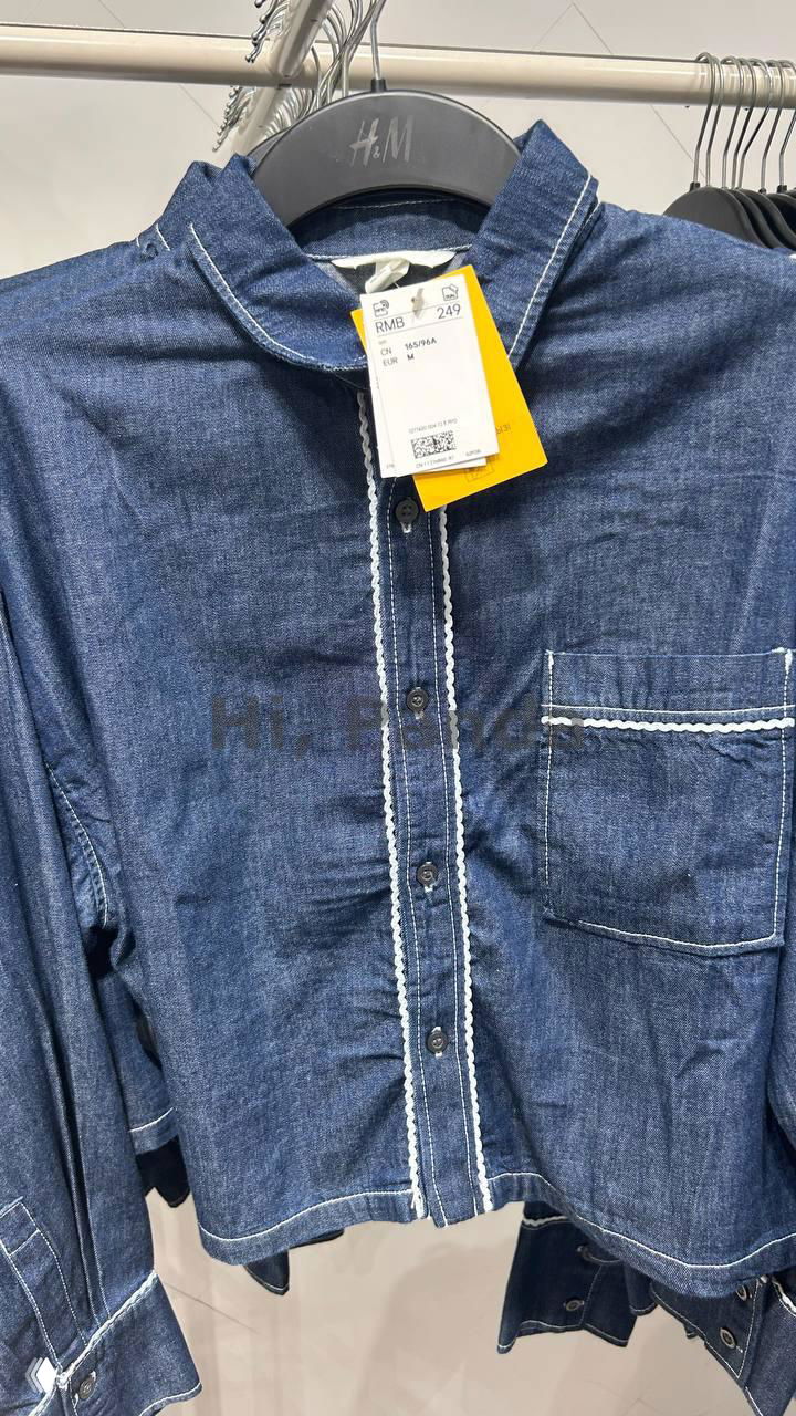 Джинсовая рубашка H&M с декоративной отделкой и видимой биркой RMB 249, висит на вешалке в торговом зале ТЦ Mangrove Tree Sanya.