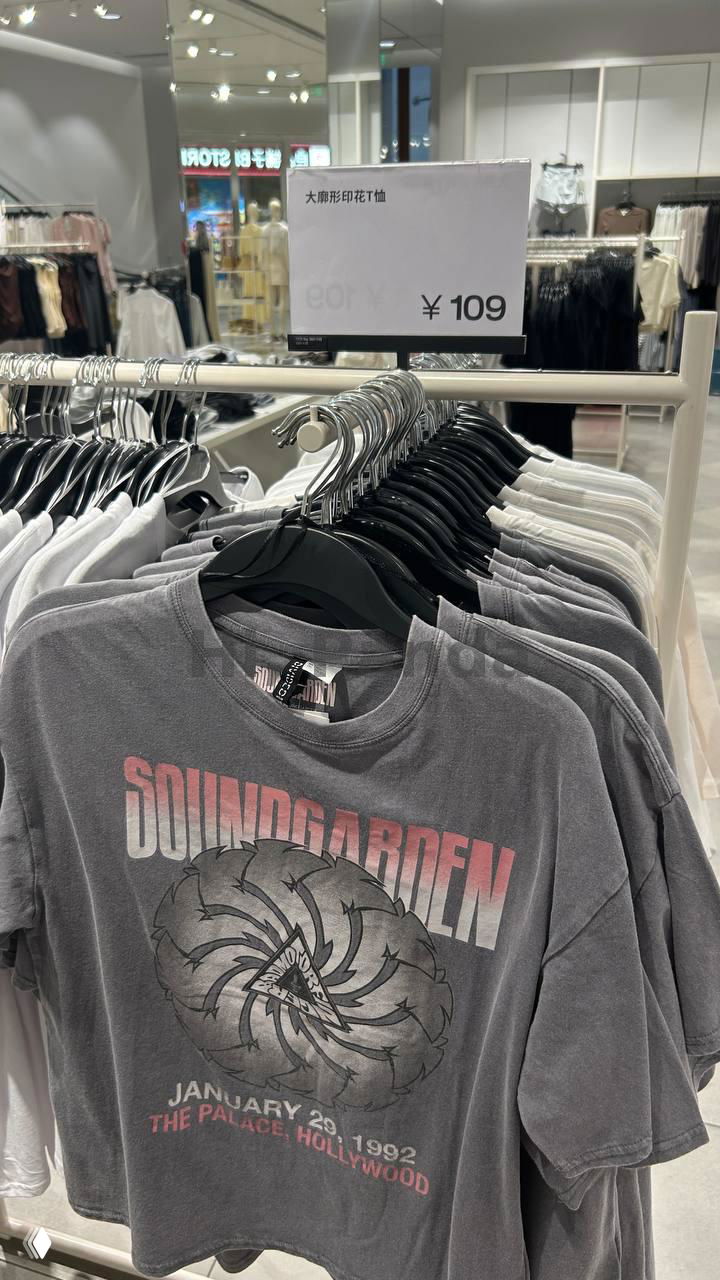 Серая футболка с принтом Soundgarden на вешалке и табличка с ценой ¥109 в задней части кадра; общая сцена торгового отдела H&M внутри торгового центра.