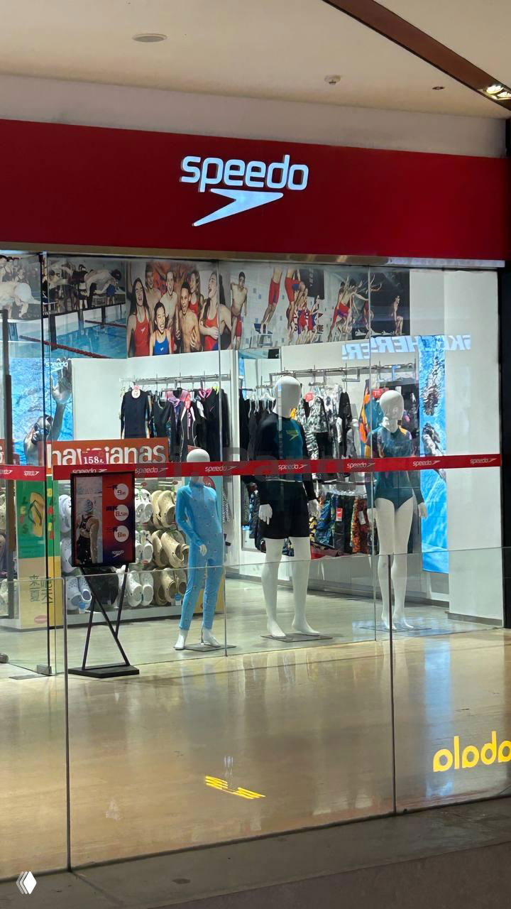 Витрина Speedo в торговом центре: манекены в купальниках, отражения в стеклянных поверхностях и внутреннее освещение магазина.