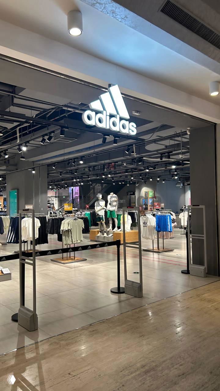 Отдел спортивной одежды Adidas в ТЦ Mangrove Tree Sanya: подсвеченный логотип adidas над входом, манекены и открытая планировка торгового зала.