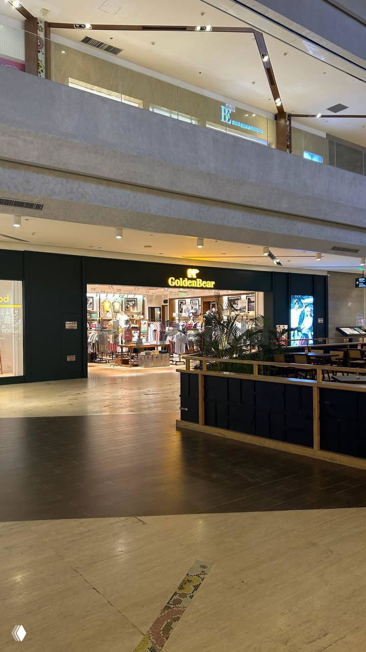 Вид галереи внутри Mangrove Tree Sanya: двухуровневая структура торгового центра и вход в магазин GoldenBear на нижнем уровне.