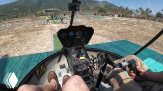 Вид из кабины вертолёта на приборную панель, ноги пилота и посадочную площадку на фоне гор и побережья на Хайнане.