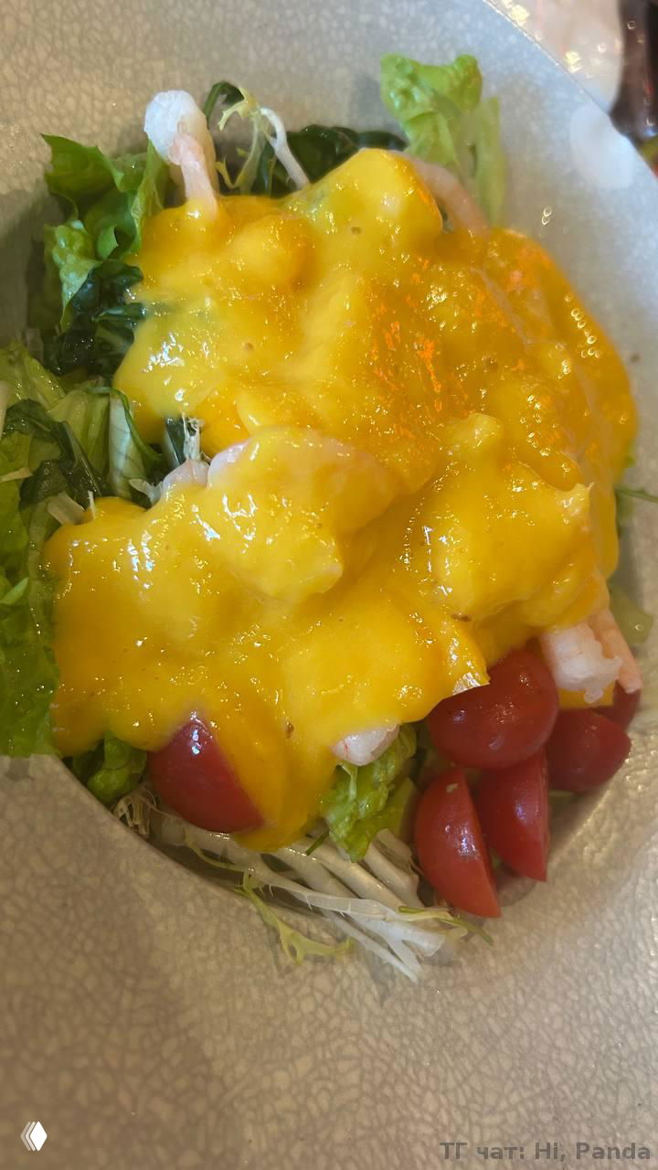 Блюдо салата с креветками и ярким манговым соусом на зелёной подложке; крупный план показывает текстуру соуса и ингредиенты.