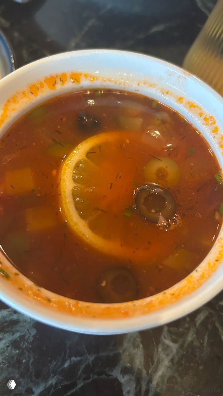 Тёплый томатный суп с маслинами и долькой лимона в белой пиале — кадр крупным планом демонстрирует цвет и ингредиенты блюда.