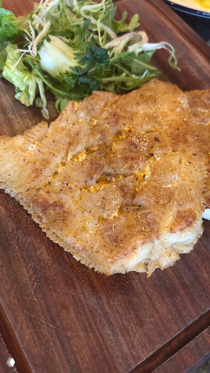 Кусок жареной рыбы или отбивная на деревянной доске рядом с салатом — крупный план блюда и текстура корочки в фокусе.