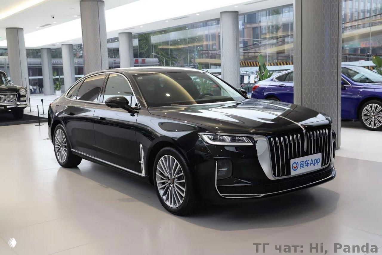 Чёрный представительский седан в выставочном зале: элегантный кузов, большая хромированная решётка радиатора и стильные легкосплавные диски вблизи.