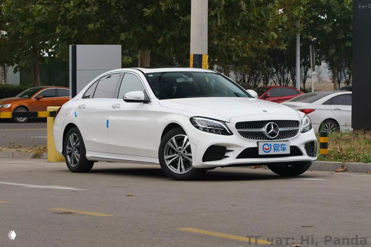 Белый седан Mercedes‑класса на городской стоянке: профиль автомобиля, линии кузова, дневные фары и общий городской фон вокруг машины.