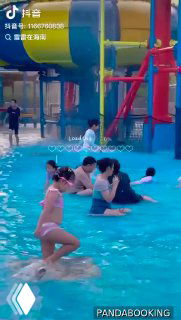 Крупный план зоны с горками и мелким бассейном: дети и взрослые играют в воде рядом с надувными и пластиковыми аттракционами, видны спасатели и персонал.