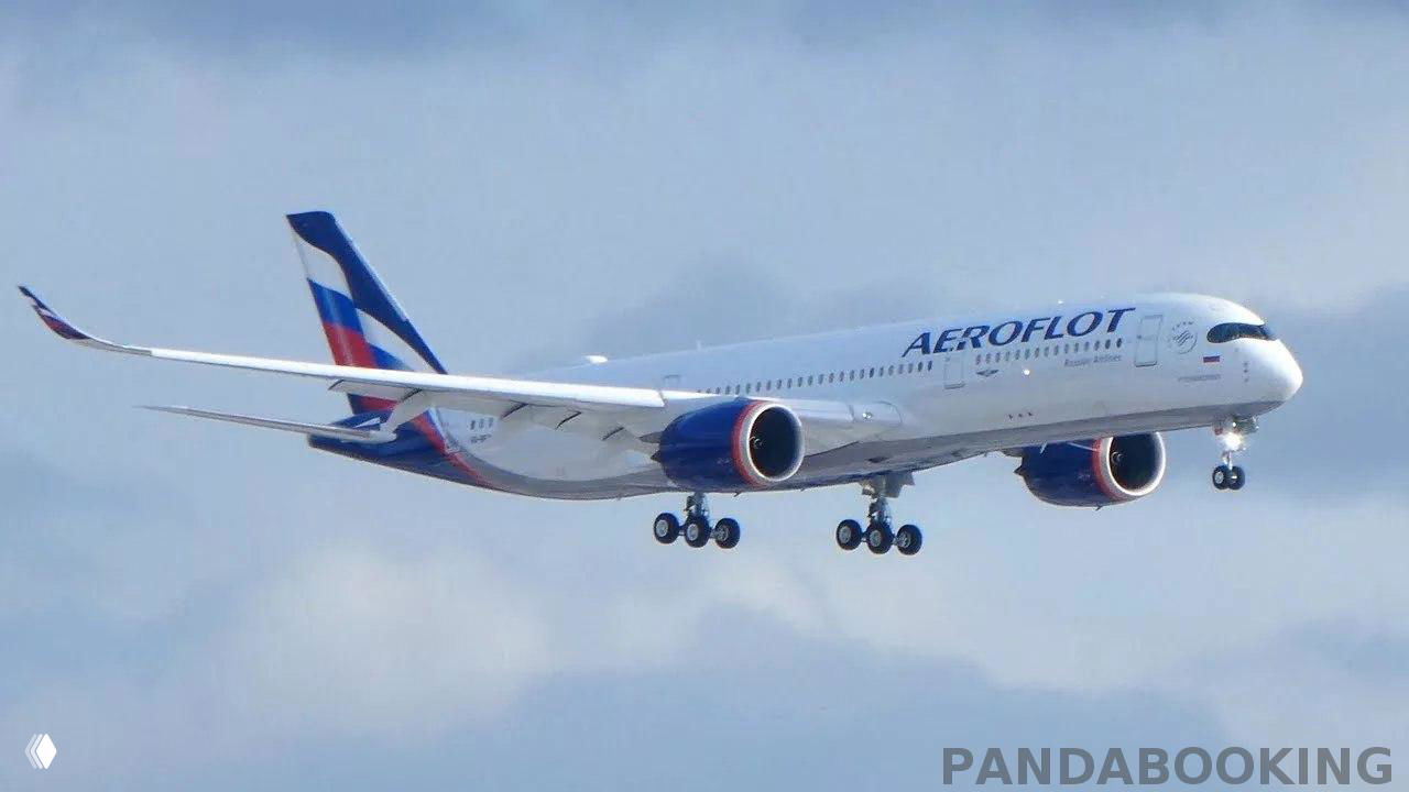 Крупный план самолёта Aeroflot в заходе на посадку над облачным небом; видно раскрытое шасси, логотип авиакомпании и водяной знак Pandabooking.