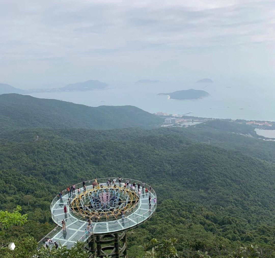 Смотровая площадка с прозрачным полом и посетителями на фоне зелёных гор и моря при пасмурной погоде — вид из парка Ялонг.