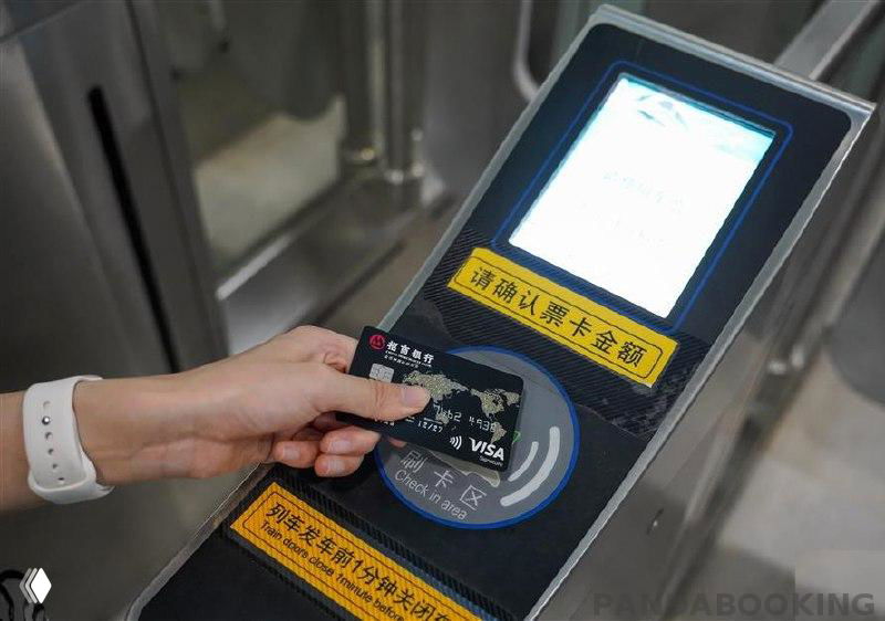 Рука прикладывает иностранную банковскую карту с логотипом Visa к считывателю турникета шанхайского метро, наглядный пример бесконтактной оплаты для туристов