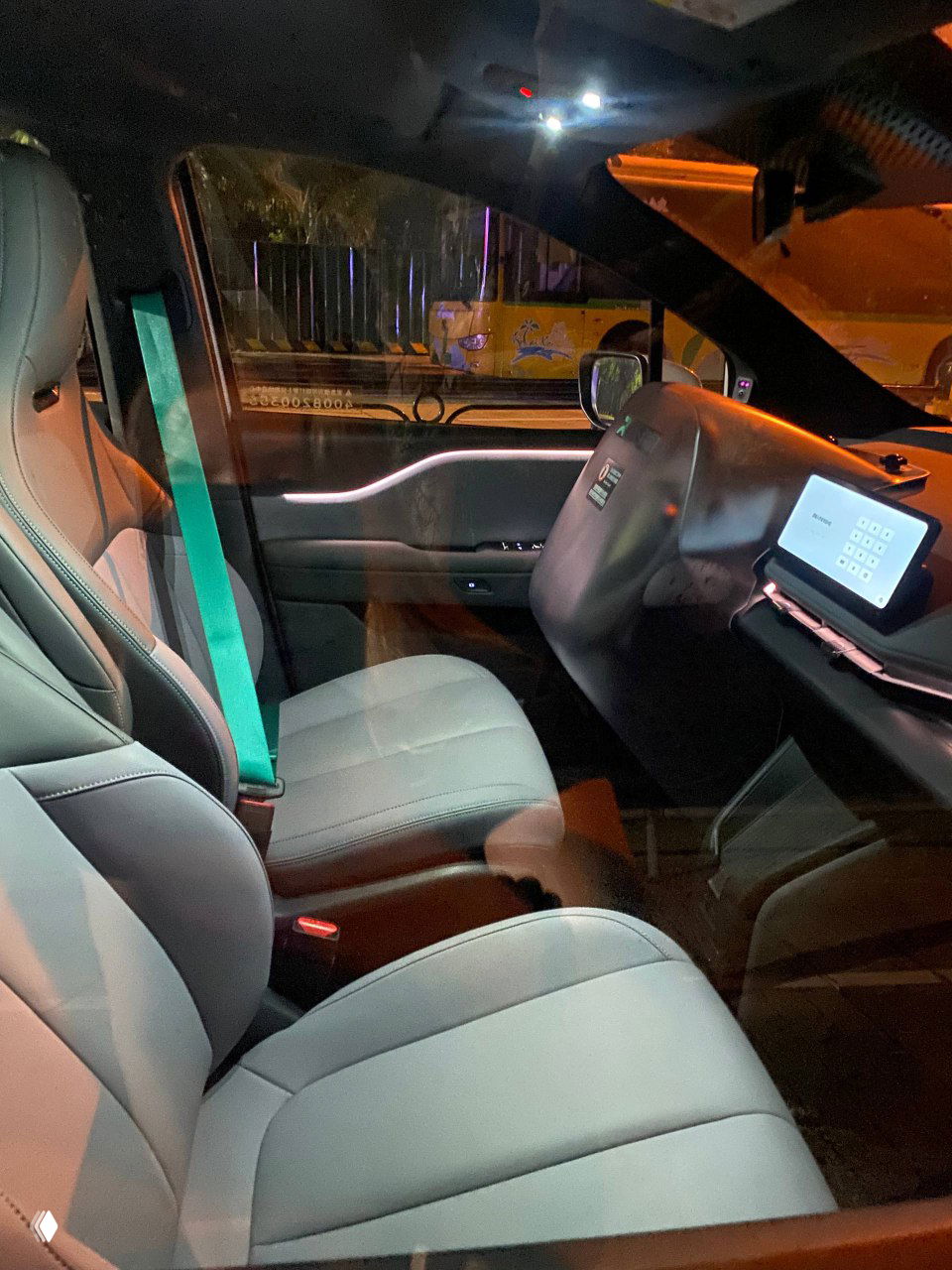 Вид через стекло на переднее пассажирское сиденье беспилотного такси с акцентом на интерьере и цифровой панелью управления, съёмка сделана вечером в городе.