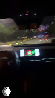 Размытый ночной кадр с видом на дорогу из салона автономного такси, видна подсветка приборной панели и городской трафик сквозь лобовое стекло.