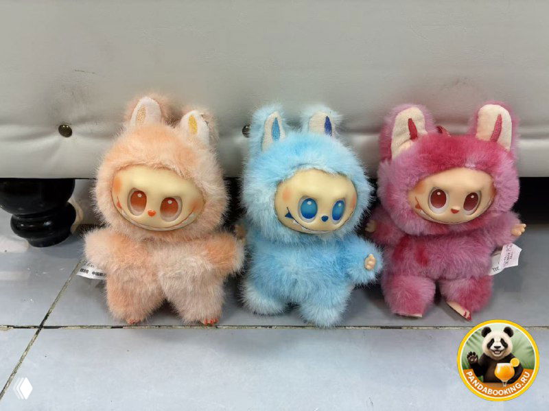 Три пушистые мягкие игрушки Labubu разных цветов — персиковая, голубая и розовая — выставлены на фоне; сувениры для выбора после экскурсии.