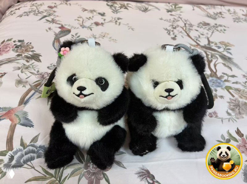 Два плюшевых брелока в виде панды на тканом покрывале; чёрно‑белые мягкие сувениры с фирменным логотипом Pandabooking.