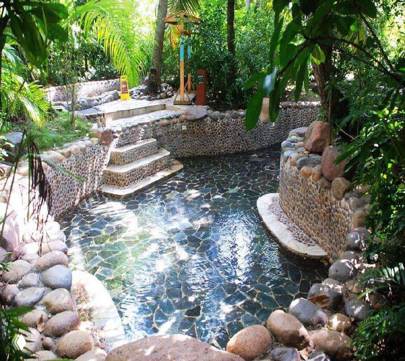 Теплый термальный бассейн на Хайнане среди тропической зелени и каменной облицовки; видны ступени и мозаичная отделка.