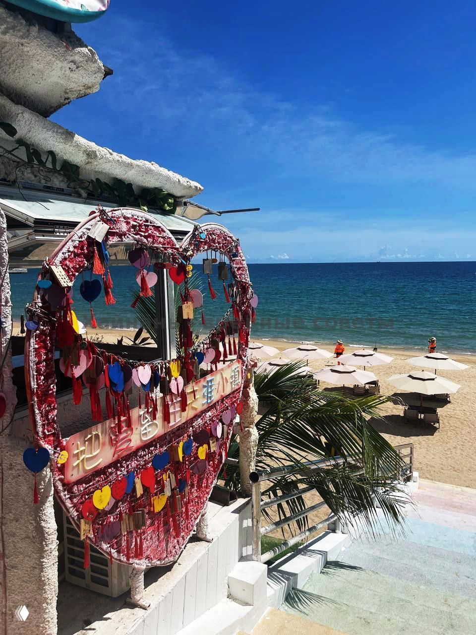 Декоративная инсталляция в форме сердца с множеством цветных бирочек и вид на пляж и море ниже — фотозона в туристической части Танья.