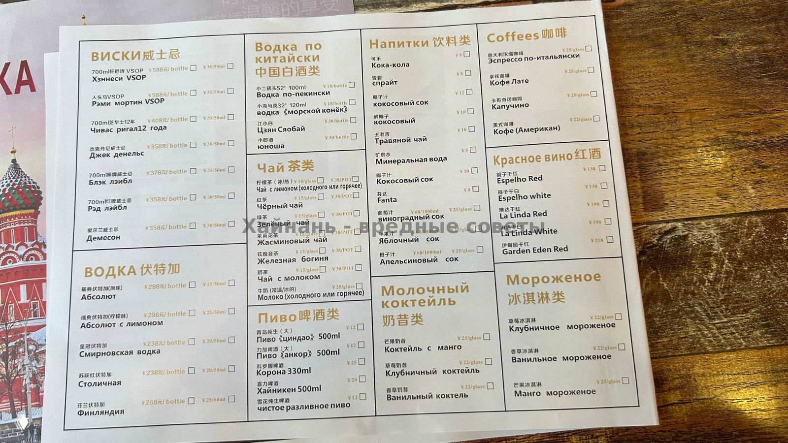 Фото меню напитков и алкоголя: разделы виски, водка, чай, пиво и кофе с ценами; лист меню разложен на деревянной поверхности, вид сверху.