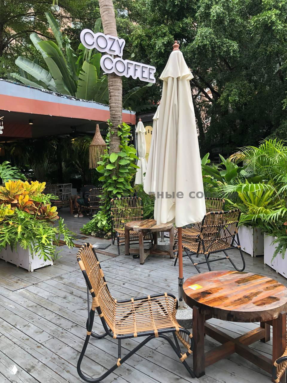 Уличная терраса Cozy Coffee: столики и кресла на деревянном настиле, зелёные растения, вывеска кафе и зонты на открытой площадке в Дадунхай.