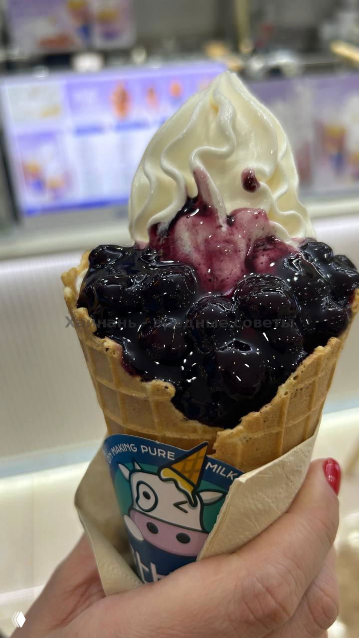 Рожок с белым мягким мороженым и густым тёмным ягодным топпингом (похоже на чернику), крупный план, мороженое в вафельном стаканчике.