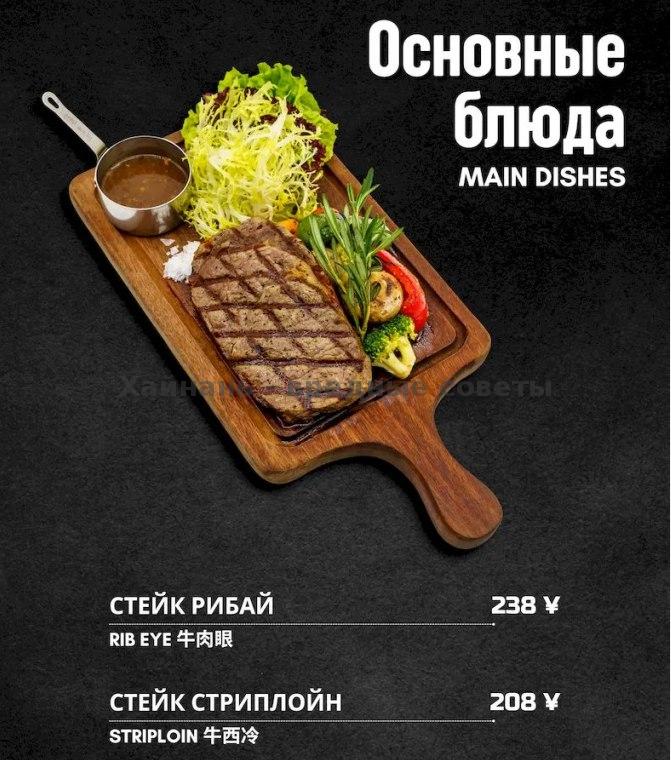 Раздел меню с фотографией стейка на деревянной доске: рубай и стриплойн с гарниром, оформление и цены в меню бара Freegen на чёрном фоне.